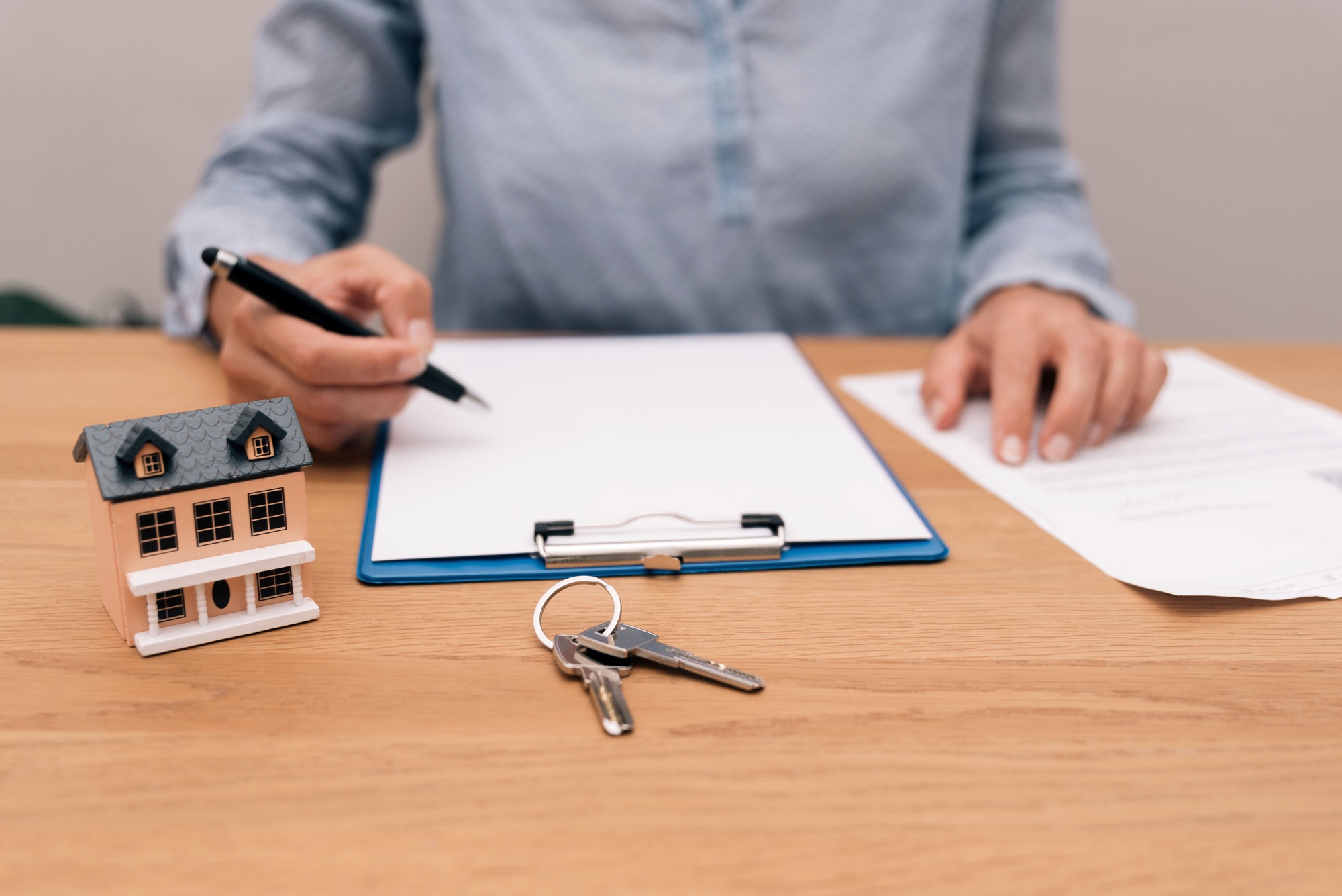 Person reviewing real estate documents with miniature house and keys on desk